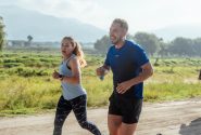 Two adults running on a rural dirt path, enjoying a sunny day outdoors.