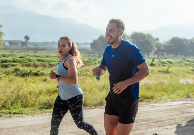 Two adults running on a rural dirt path, enjoying a sunny day outdoors.